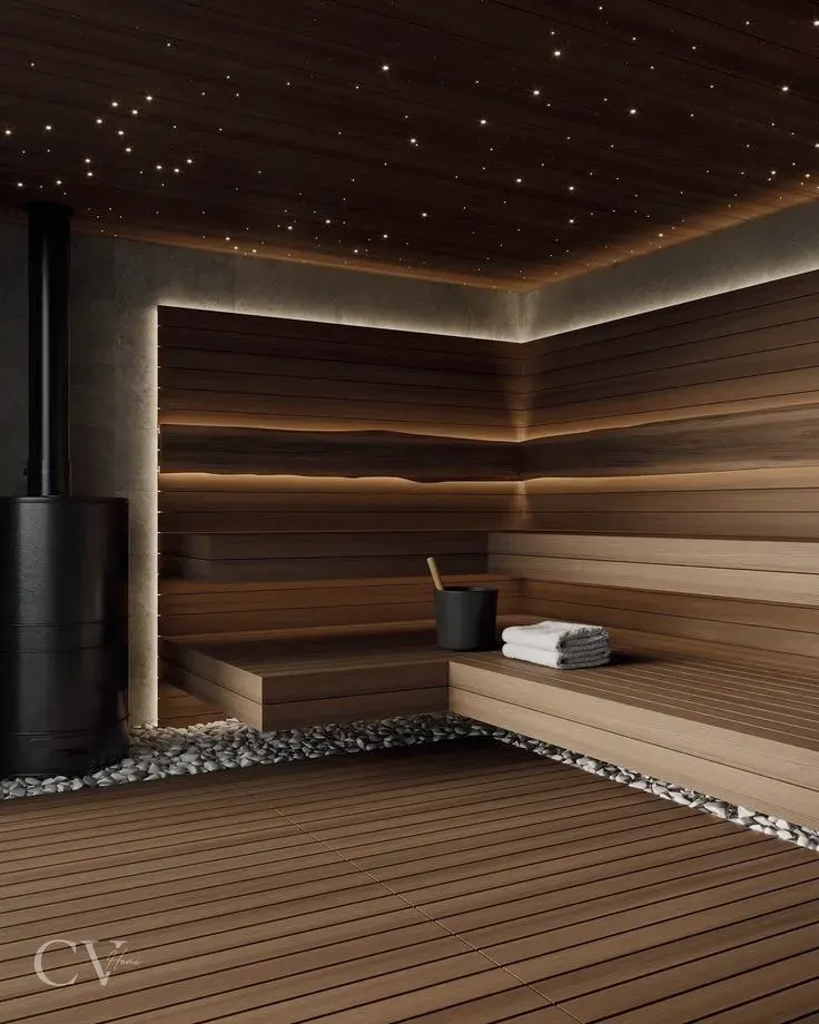 Tünd rəngli müasir sauna dizaynı: küncdə qara silindrik soba, daş döşəmə zolağı və işıqlandırılmış oturacaqlar
